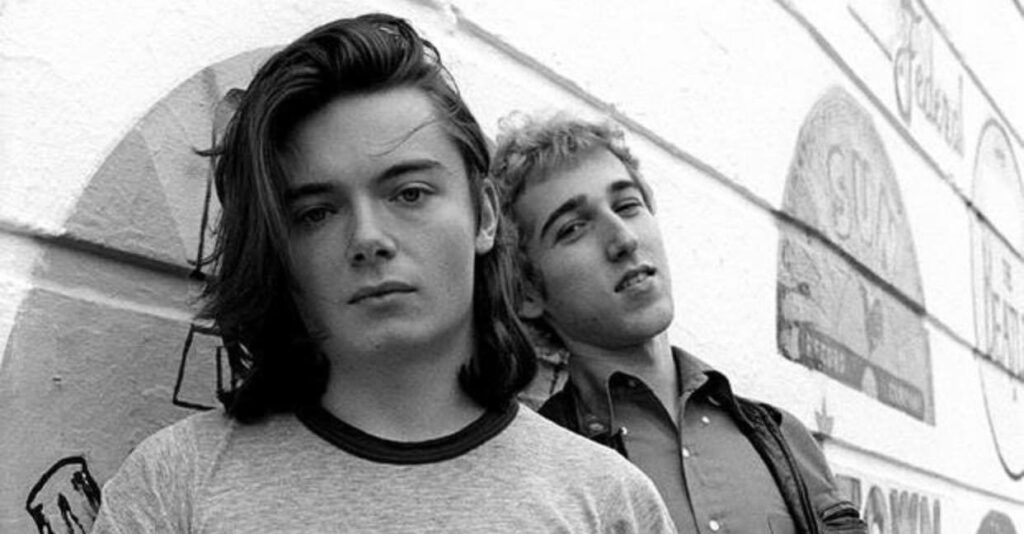 Portrait en noir et blanc de Thomas Bangalter et Guy-Manuel de Homem-Christo jeunes, posant sans masque contre un mur orné de logos de labels de musique.