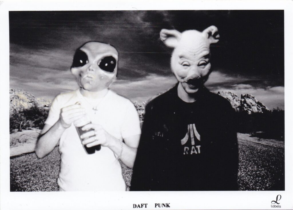 Photo promotionnelle en noir et blanc de Daft Punk en 1995 portant des masques de plastique (un alien et un cochon) pour la sortie du single "Da Funk".